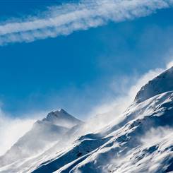 Wolken rollen über schneebedeckte Bergen bei klarem Himmel