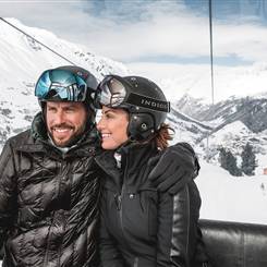 Paar in Skioutfit und Helm in einer Gondel
